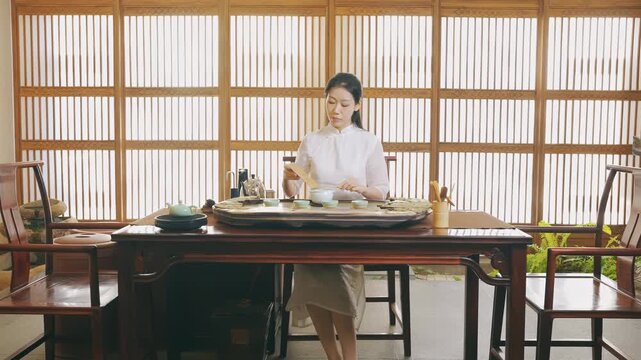 Young woman tea master preparing traditional ceremony chahe with black tea brewing technique over the table for serving guests in classic teahouse for relaxing cultural experience with teapot teacup