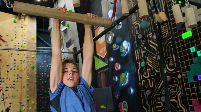 Boy hung on horizontal bar in sports center. Young athlete uses last strength avoiding from falling to improve endurance slow motion