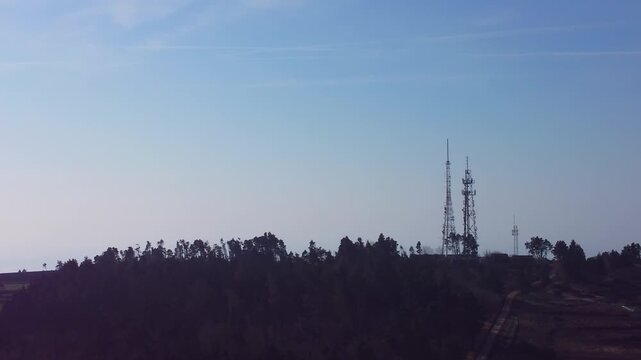 TV Radio 5G Transmitter Towers on Hilltop with Silhouetted Trees. Broadcast Television and Mobile Smart Phone Infrastructure.
