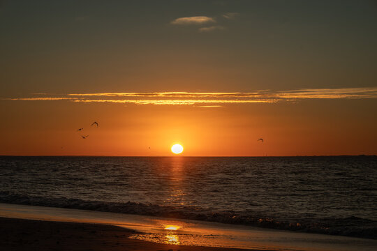 un amanecer donde se pinta el paisaje de color naranja ,  un mar azul , cielo celeste , nubes naranjas , en vuelo varios gaviotas , un horizonte que invita a estar mirandolo 