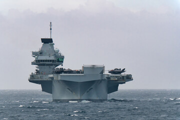 Royal Navy aircraft carrier HMS Prince of Wales sailing in Tokyo Bay, Japan, with F-35B fighter jets on deck, rough and cloudy weather. © zapper