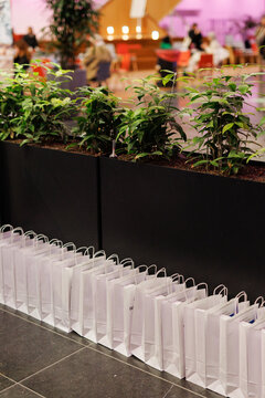 Neatly arranged goody bags prepared for visitors at a fair or corporate event, with a caf&eacute; setting and people in the background. Ideal for themes of marketing, branding, hospitality.