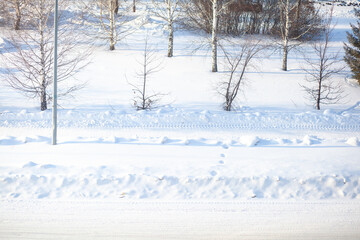 Fototapeta premium Snow-covered landscape with bare trees and tire tracks on a road under clear blue sky in a winter setting