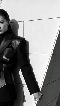 Vertical video: Holding angled panel, model in black blazer shifting hand, sunlight hitting facade