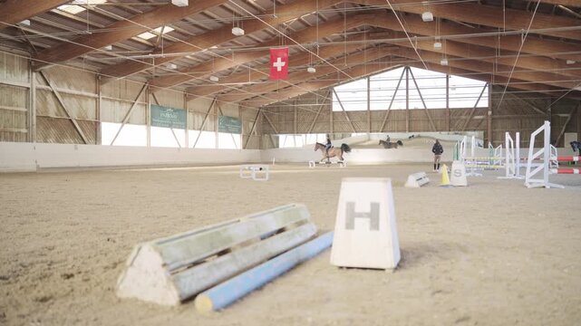 Riders training with their horses on a show jumping course inside a large riding hall