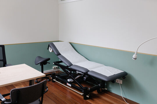 Clean and modern GP doctor&rsquo;s office corner with examination chair, desk, and dark wood flooring.