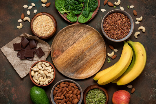 High magnesium foods and empty wooden plate, top view, flat lay, dark grunge background.