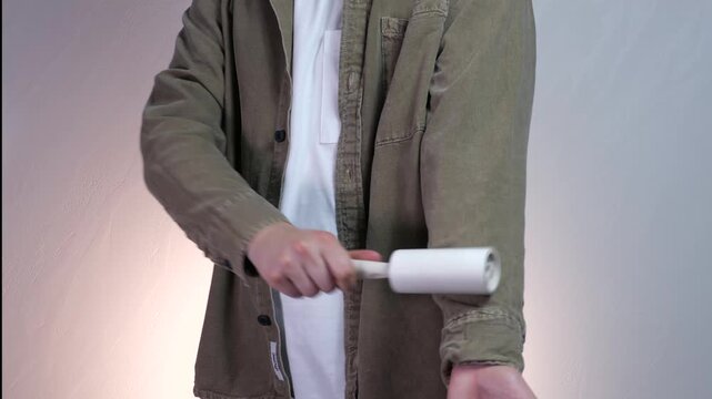 Person using a sticky lint roller to remove dust and pet hair from clothes. High-quality footage for household hacks, garment maintenance, and textile care commercials. Clean, bright lighting and