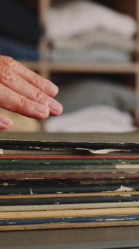 Vertical video: Grasping stack, hands shifting grip, fanning worn sleeves on table for sorting