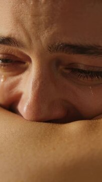 Vertical video: Leaning woman pressing face into forearm on couch, suppressing sobs, shedding tears