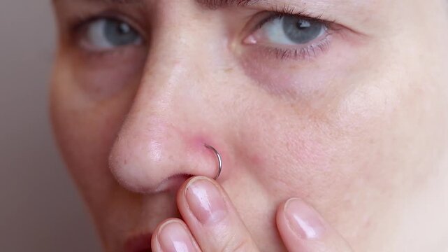 woman suffers and experiences pain from a nose piercing.. Inflamed piercing, nose after piercing. Red nose piercing site. Close up footage