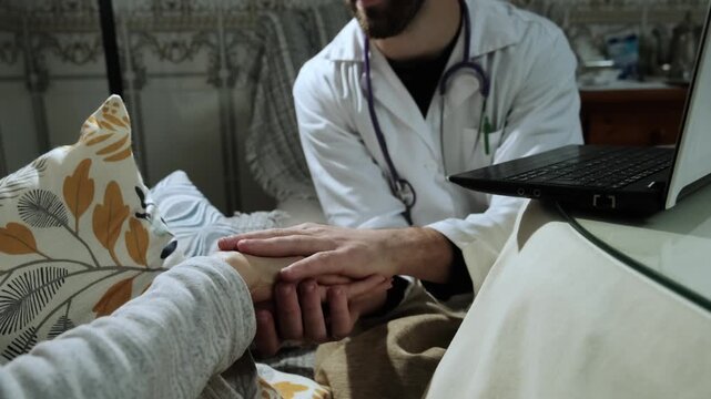 Caring male physician holding and reassuring a patient's hand during a medical house call. Professional healthcare and support at home