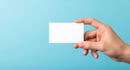 Fototapeta premium Hand holding blank white card against a bright blue background image