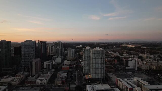 Drone pulling back over downtown San Diego at sunset with an airplane descending toward the airport in the background.