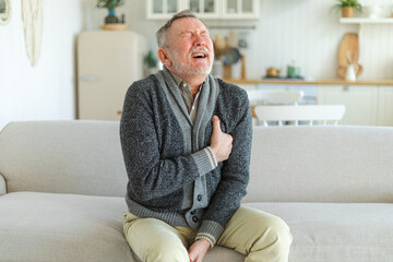 Fototapeta premium Pain on heart, heart attack. Unhappy middle aged senior man suffering from chest pain heart attack problems with health at home. Mature old senior grandfather touching chest experiencing infarction
