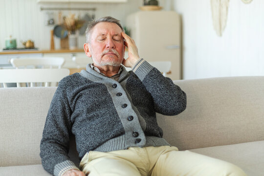 Headache pain. Unhappy middle aged senior man suffering from headache sick rubbing temples at home. Mature old senior grandfather touching temples experiencing stress. Man feeling pain hurt in head