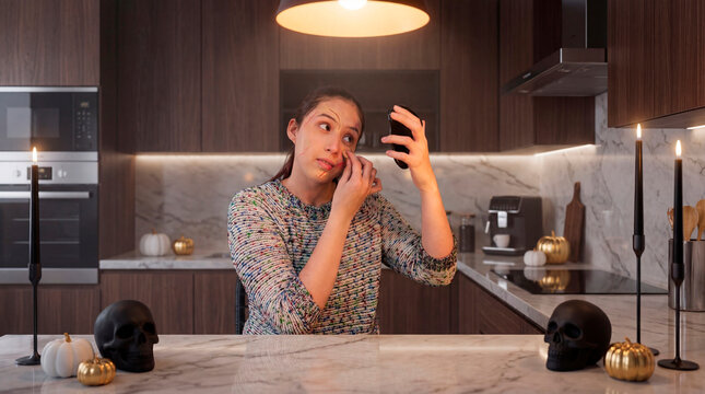 Methodical woman removing Halloween makeup in modern kitchen