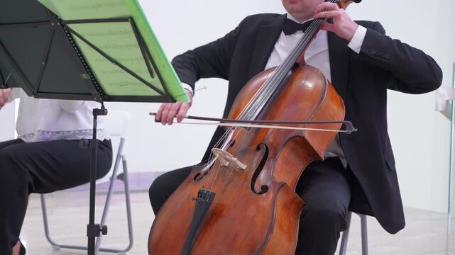 Cellist playing classical music. Close-up of hands on strings, bow movement, and instrument details. Elegant black suit, studio lighting, music production background.