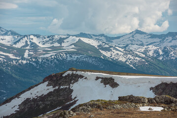 Scenic view from sunlit gold stone outcrops and sharp golden rocks to pointy peaks and peaked tops under cloudy sky. Wild rugged alpine landscape with snow cornice and rocky snowbound mountain range. © Daniil
