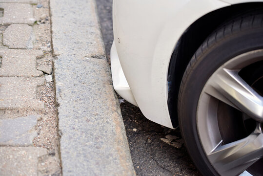 White vehicle spoiler positioned dangerously close to granite sidewalk curb during precision parking in an urban environment. Car parked close to the curb. Low clearance.  Selective focus