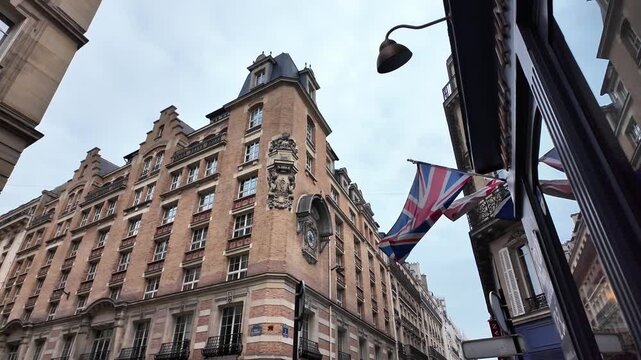 Low angle static shot of the British Union Jack flag waving from a traditional Parisian stone building under an overcast