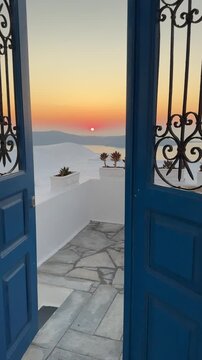 Beautiful sunset in Santorini island, Greece. Passing through the blue door to the terrace. White architecture and sea view at sunset. Travel and summer vacation concept. Vertical video

