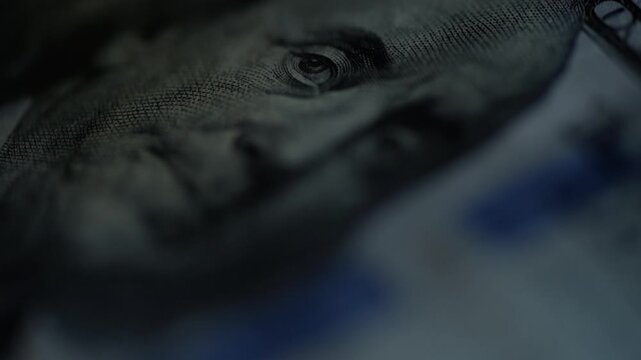 Hundred dollar bill closeup flicker, intense forensic lighting reveals paper fiber, security stripe, microprinting, shallow depth of field, slow camera sweep, moody blue shadows,