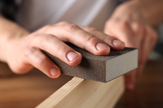 Man polishing wooden plank with sanding block at table, closeup