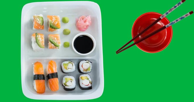 Overhead view of sushi in a plate , bowl and chopsticks on black surface