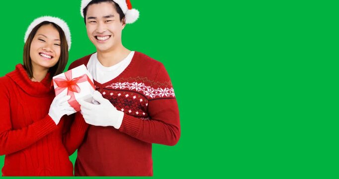 Portrait of asian couple wearing santa hats holding a christmas gift against black background