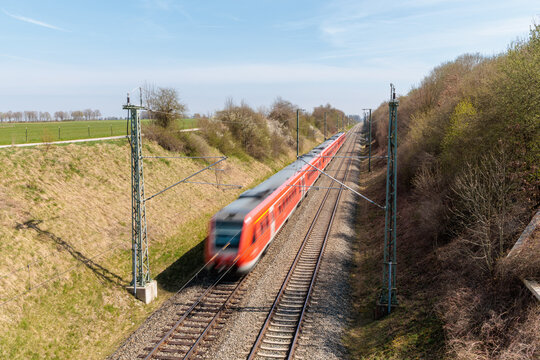 Red passenger train traveling on a railway track with motion blur, high angle view of a regional train in rural Germany, concept of public transportation and infrastructure