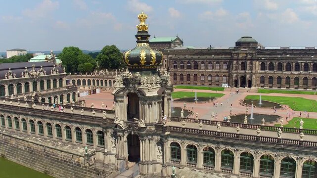 An aerial view of the Dresden Zwinger palace showing the iconic Crown Gate, the inner courtyard with fountains, and the Semper Gallery under a partly cloudy sky.