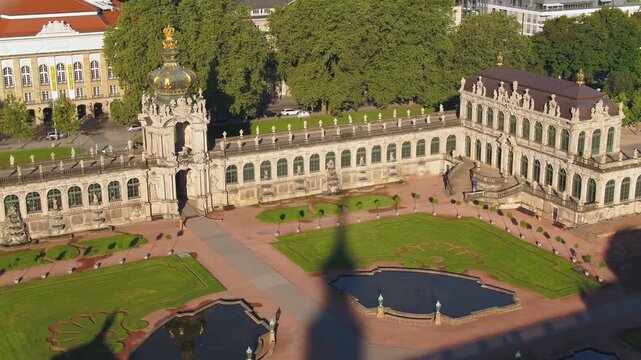 A panoramic aerial view of the Dresden Zwinger complex in golden light, featuring the complete courtyard, the Crown Gate, and the old town in the background.