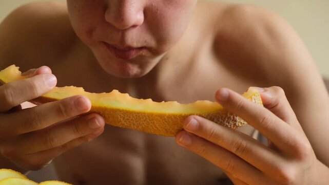 Young boy hungry greedily bites juicy flesh of melon from slice. Teen eats ripe melon and juice drips on his hands. Nutrition and healthy lifestyle. Fruit diet. Vegetarian diet.