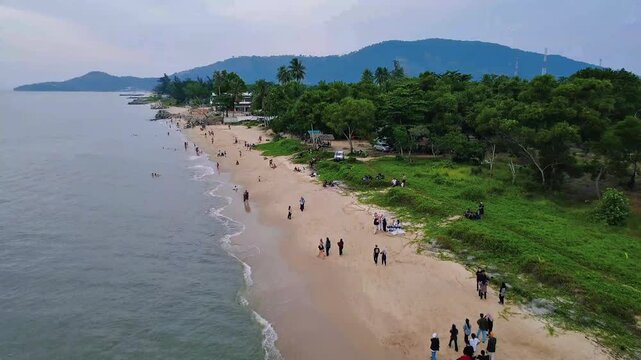 Drone view of beach with forest shoreline and small crowds