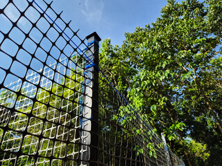 Low angle view of black mesh fence with green trees and blue sky background © Hendra Susanto0311