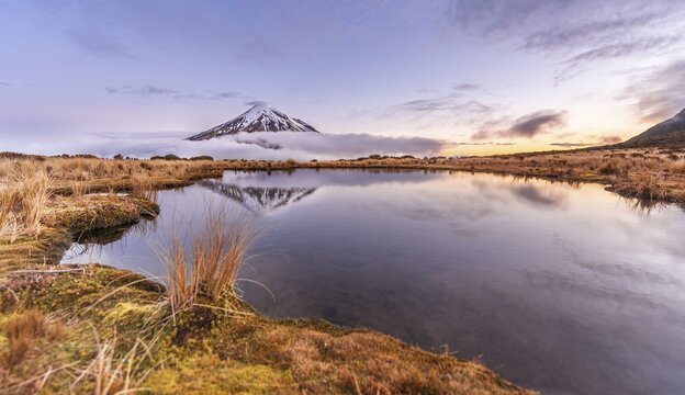 Reflection in Pouakai  Tarn lake, clouds around stratovolcano Mount Taranaki or Mount Egmont at sunset, Egmont National Park, Taranaki, New Zealand