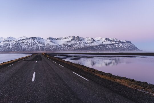 Ring road, country road by the sea, rugged volcanic landscape, mountains with snow, sunset, Iceland