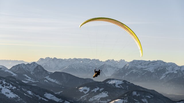 Paragliding in the air in front of a snow-covered Alpine chain in winter, Brixen im Thale, Tyrol, Austria