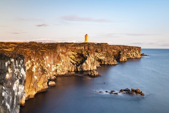 Orange lighthouse of &Ouml;ndverdarnes stands at cliff coast, rocky coast of lava rock, long time exposure, &Ouml;ndver&eth;arnes, Sn&aelig;fellsj&ouml;kull National Park, Snaefellsnes Peninsula, Sn&aelig;fellsnes, Vesturland, Iceland