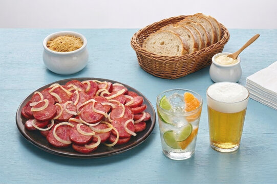 Lingui&ccedil;a Acebolada com Cerveja e Caipirinha sobre mesa de madeira azul