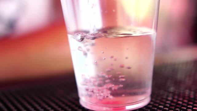 Cocktail pouring blueberries being added into a clear plastic cup on a bar mat for a refreshing party beverage