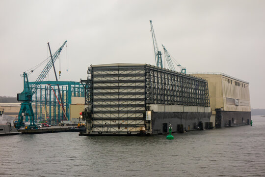 Giant floating dry dock at an industrial shipyard with harbor cranes. Concept for maritime engineering, naval construction, and global shipping logistics.