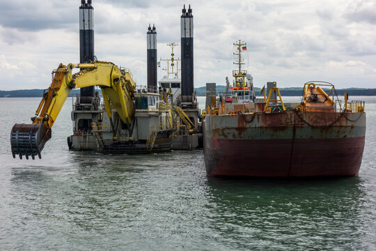 Large Dredging Vessel with Excavator Working in Harbor. Marine Construction Barge Performing Seabed Dredging for Port Development and Industrial Waterfront Projects