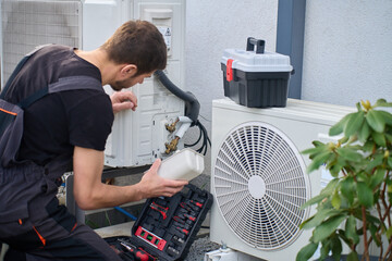 Technician servicing outdoor heat pump unit with tools beside residential house. Concept of HVAC...