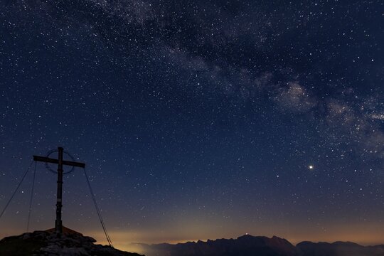 Night sky with stars and milky way over Ammergau mountains, in the foreground summit cross of the Geierkopf with tent, Reutte, Ammergau Alps, Tyrol, Austria