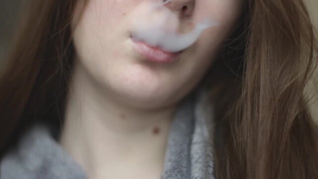 Young girl blows smoke from her mouth using an electronic cigarette. Mouth close up view