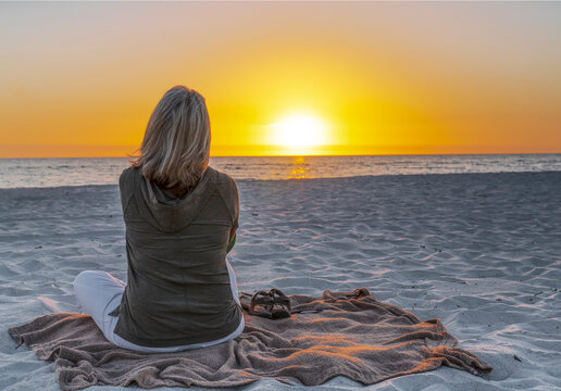 Woman from behind sitting on the beach during winter in florida watching a sunset
