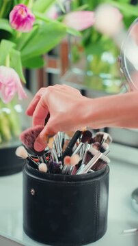 Close-up of woman hand selecting makeup brush from organized cosmetic set in black leather case. Clean beauty and minimal makeup routine preparation on dressing table with natural aesthetic.