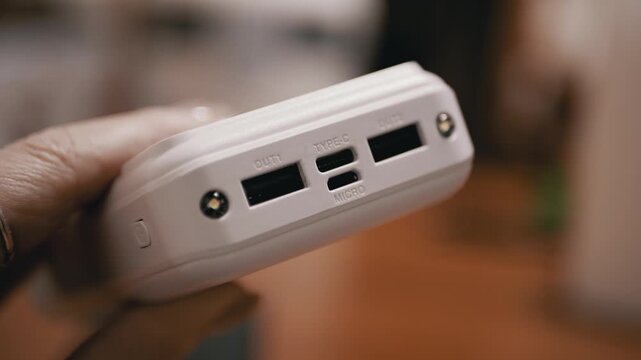 A close-up view of a hand holding a white portable power bank, displaying multiple charging ports including USB and Type-C. Concept of mobile energy, backup power, and modern tech.
